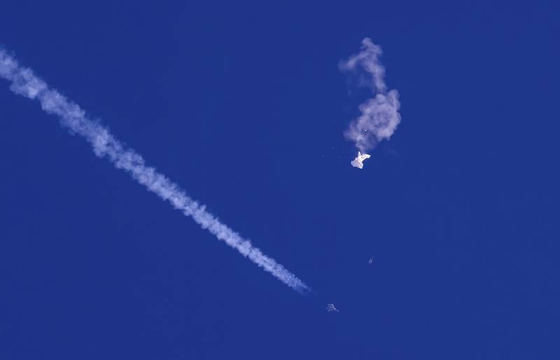 In this photo provided by Chad Fish, the remnants of a large balloon drift above the Atlantic Ocean, just off the coast of South Carolina, with a fighter jet and its contrail seen below it, Feb. 4, 2023.